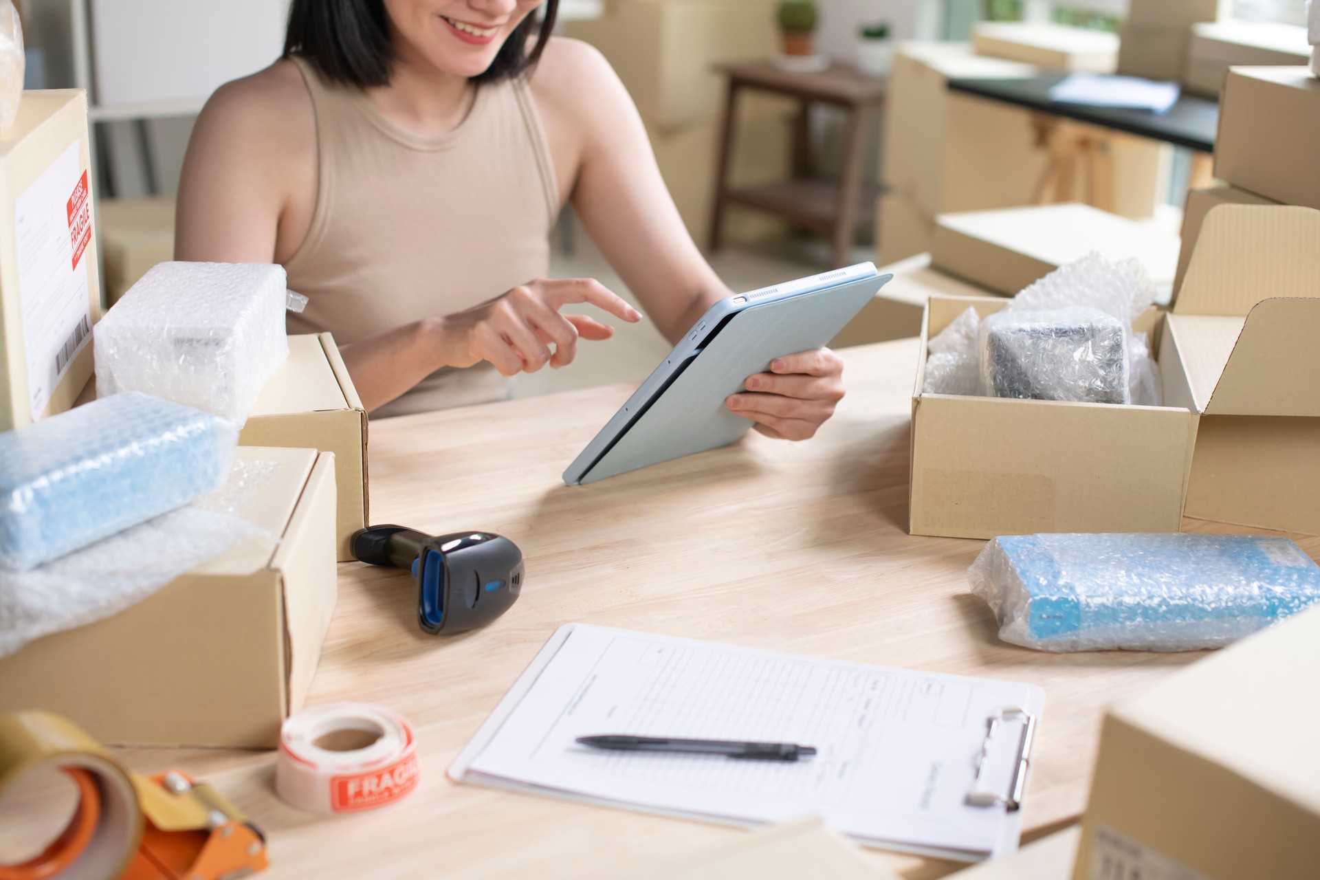 Asian woman online seller confirming orders from customer on the tablet. E-commerce business owner using tablet in store warehouse.